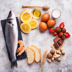Fish, prawns, lemons, honey, eggs, cream, strawberries, chocolate, nuts, wheat and bread on table