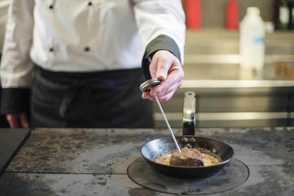 Chef taking temperature for steak in frying pan