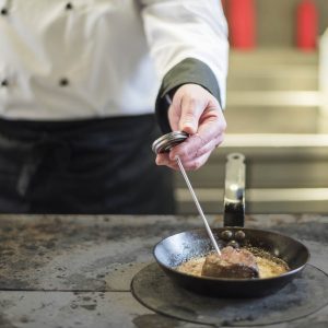 Chef taking temperature for steak in frying pan