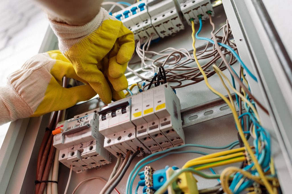 Hands in safety gloves working on fuse box