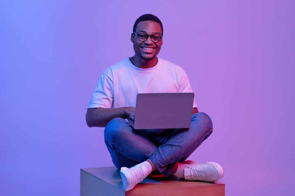 Person sitting crossed legs with a laptop against a purple background