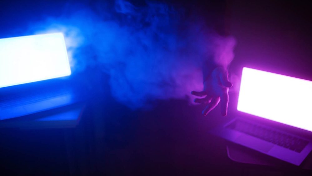 Smoky room lit by two computer screens, hand of person in smoke