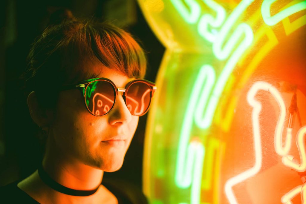 portrait of a person wear glasses next to neon sign
