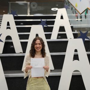 Madeleine holding results, large a's in background on stairs.