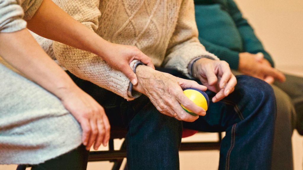 older hands holding a ball, with younger hands gently holding arm