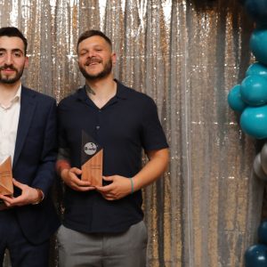 Haidar (left) and Daniel (right) holding their trophies in front of a silver sparkly background