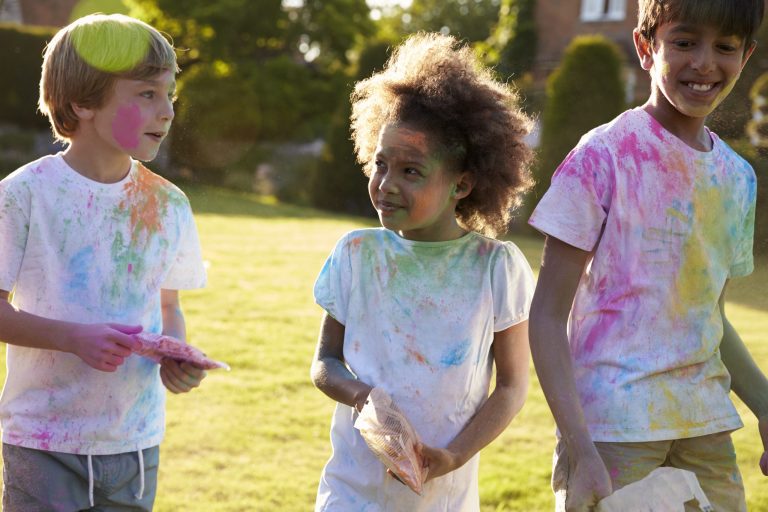 Three children playing with Holi paint.