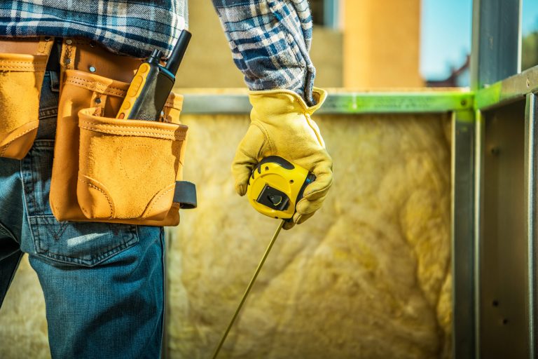 Back of a workman with tools in belt and a tape measure in hand.