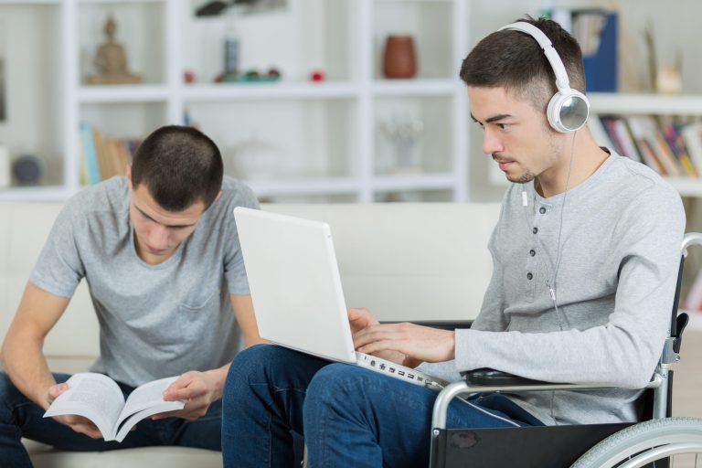 Two people, one reading, one in a wheelchair on a laptop wearing headphones.