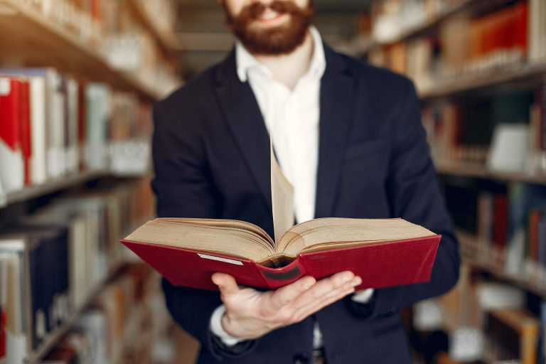 Person reading a book with library background.