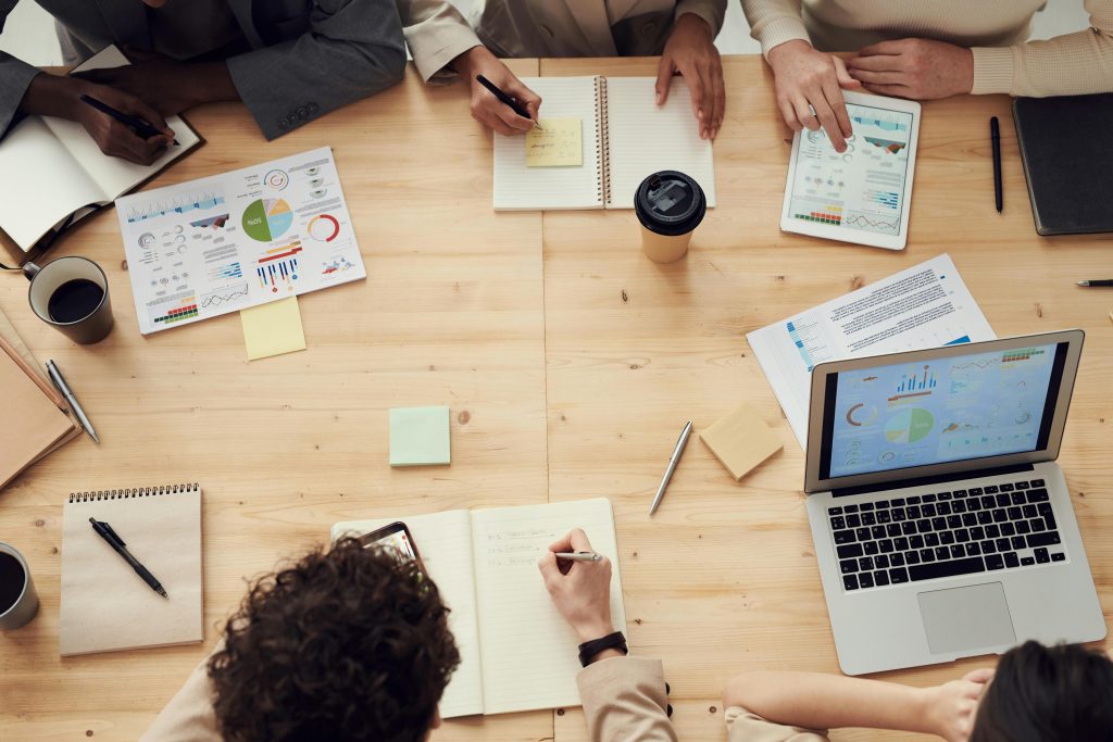 Group of people sitting around a table with notebooks and laptops