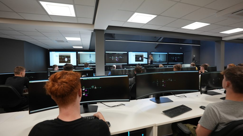 Pembrokeshire college learner looking at the screen in the Control Room. Teacher at the front of the class