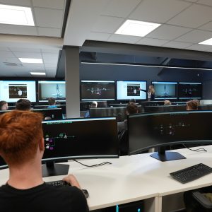 Pembrokeshire college learner looking at the screen in the Control Room. Teacher at the front of the class