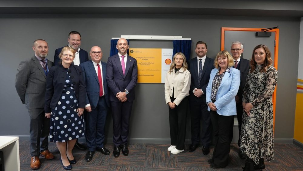 Two groups of people standing either side of yellow and white plaque at the opening of Shell Hub.