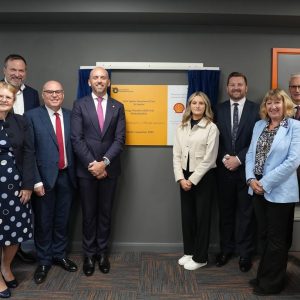 Two groups of people standing either side of yellow and white plaque at the opening of Shell Hub.