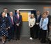 Two groups of people standing either side of yellow and white plaque at the opening of Shell Hub.